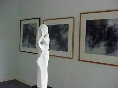 Ausstellungsraum mit einer hohen weißen Skulptur und gerahmten dunklen Gemälden