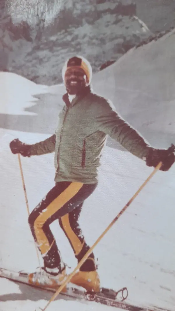 Farbfoto aus den 1970er Jahren: Johnson lachend auf Skiern, in grüner Jacke und gestreifter Skihose mit Wollmütze