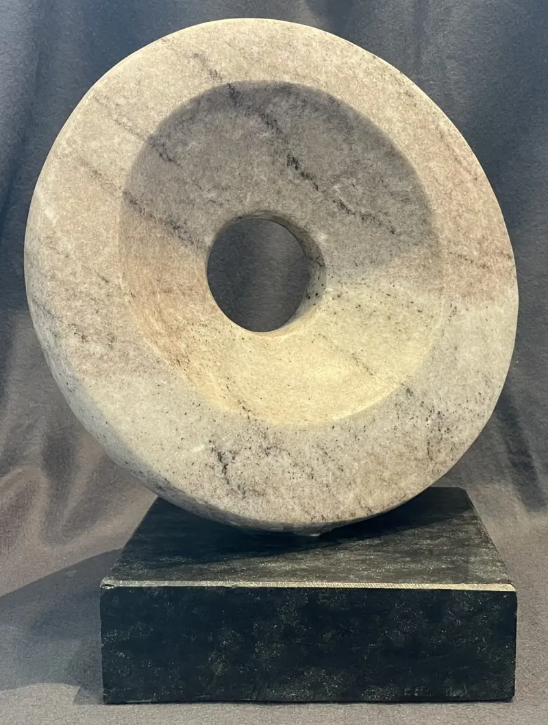 Ringförmige Skulptur aus hellem, grau geädertem Marmor auf dunklem Steinsockel