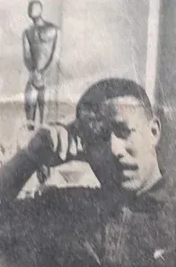 Zeitungsfoto von 1968: Ronald E. Johnson, die Hand an der Stirn, vor einer stehenden Holzfigur